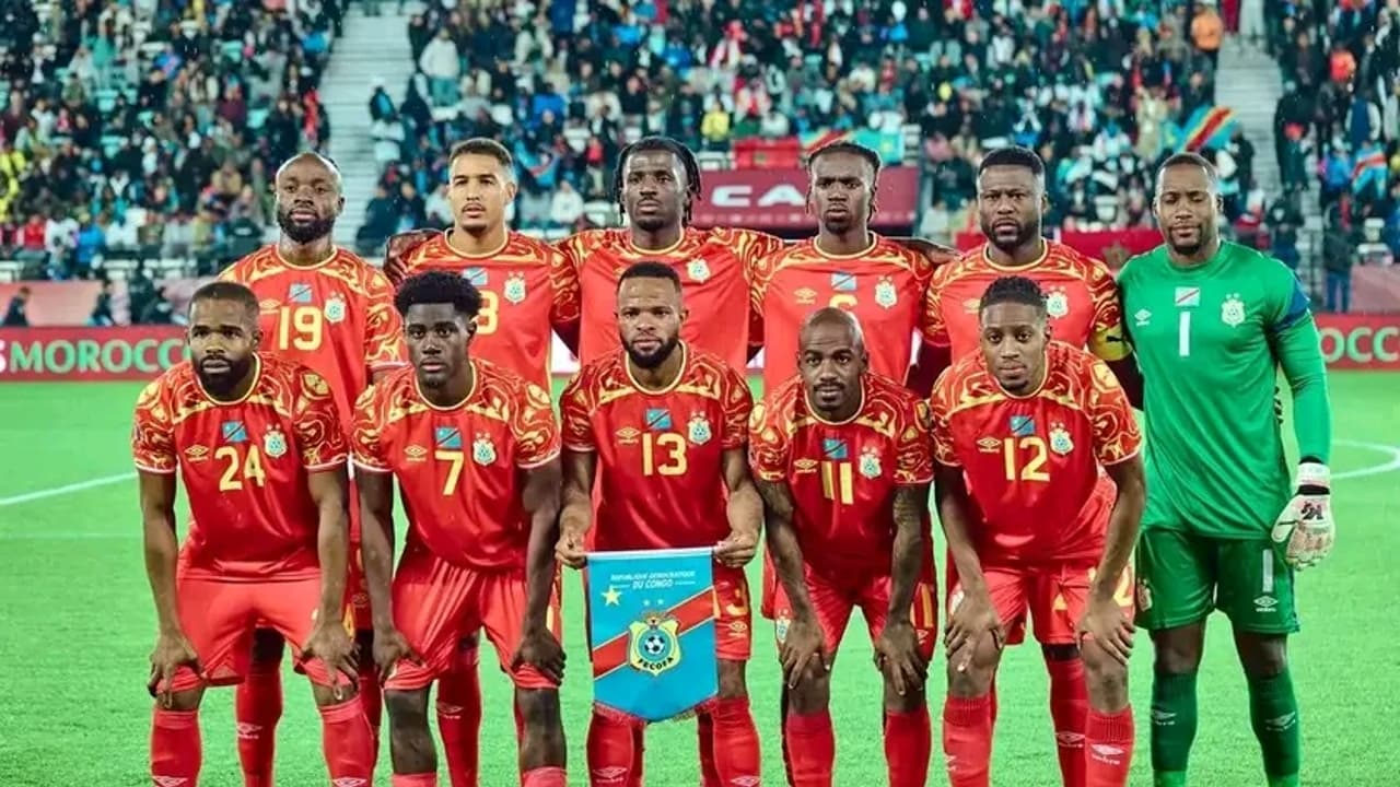 Le onze de départ de la sélection congolaise de football, en maillot rouge, posant sur la pelouse d'un stade avant le coup d'envoi, le gardien en vert à droite.