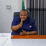 Daniel Bumba Lubaki, gouverneur de la ville de Kinshasa, assis à son bureau, la main levée, devant un chevalet portant son nom et son titre, entre le drapeau de la RDC et celui de la ville de Kinshasa.
