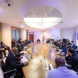 Vue d'ensemble d'une salle de réunion du ministère des Mines à Kinshasa, où des dizaines de représentants de sociétés minières sont assis autour d'une grande table ovale, devant le drapeau congolais et le portrait du chef de l'État.