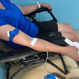 Une donneuse allongée sur un lit de prélèvement, le bras garrotté et perfusé, tandis qu'un agent de santé maintient la poche de sang posée dans une bassine bleue au sol, au Centre de transfusion sanguine de Beni.