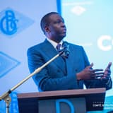 André Wameso, gouverneur de la Banque centrale du Congo, s'exprime debout au pupitre devant un micro lors d'une conférence de presse du Comité de politique monétaire, le logo de la BCC projeté derrière lui