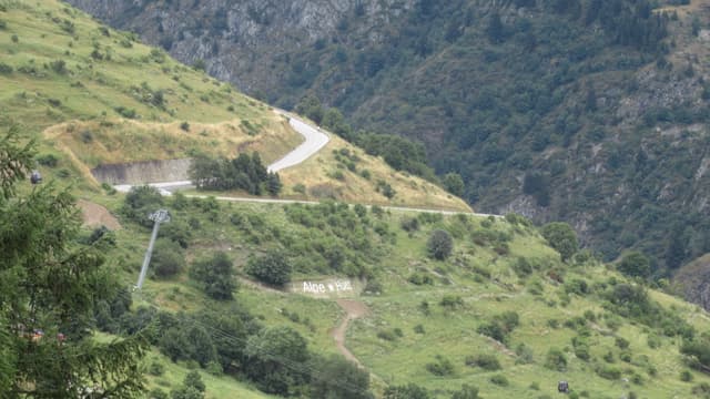 Les lacets en épingle de la montée de l'Alpe d'Huez à flanc de montagne, avec l'inscription « Alpe d'Huez » sur la pente et des cyclistes sur la route lors d'une étape du Tour de France.