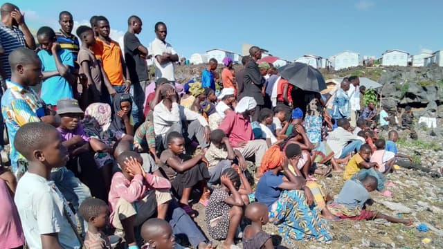 Foule de déplacés congolais, hommes, femmes et enfants, assis à même le sol rocailleux devant des abris de fortune sur un site de déplacés dans l'Est de la RDC.