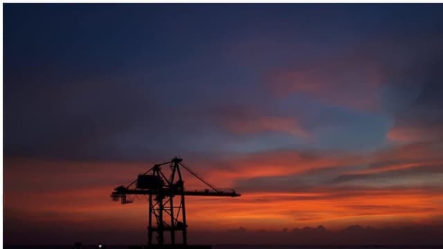 Silhouette d'une installation pétrolière offshore dressée en pleine mer, se découpant sur un ciel embrasé au coucher du soleil