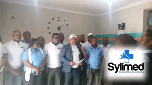 Des responsables du Syndicat libre des médecins (SYLIMED), en polos bleus, entourent un porte-parole lisant une déclaration au micro lors d'un point de presse à Kinshasa