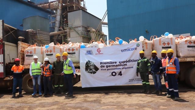 Des agents en tenue de travail posent devant une bannière STL, Gécamines et Umicore marquée « Première expédition de germanium », devant les big-bags de concentré chargés sur un camion et l'usine du Terril de Lubumbashi.