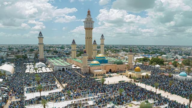 Vue aérienne de la grande mosquée de Touba, avec son grand minaret Lamp Fall et ses coupoles vertes et dorées, entourée d'une foule immense de pèlerins mourides rassemblés sur l'esplanade lors du Grand Magal.