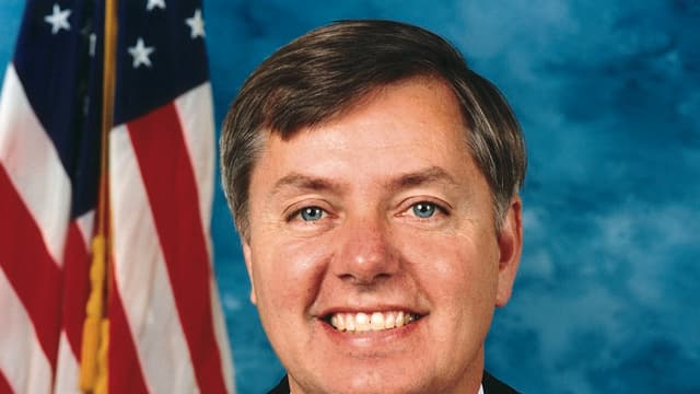 Portrait officiel du sénateur américain Lindsey Graham, en costume sombre et cravate, devant les drapeaux des États-Unis