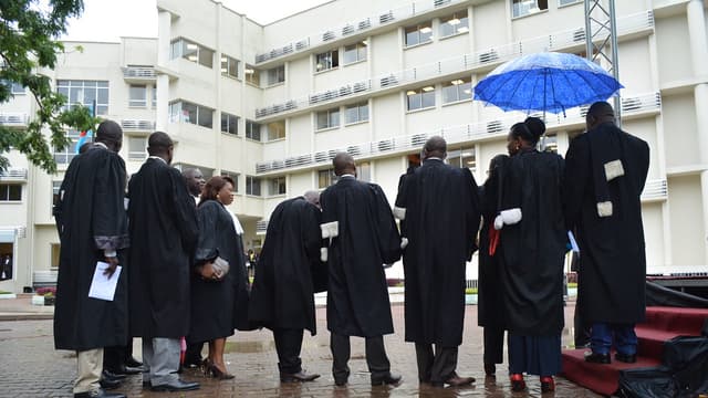 Un groupe de magistrats congolais en robe noire, réunis dans la cour intérieure du nouveau Palais de justice de la commune de la Gombe, à Kinshasa, devant un bâtiment moderne de plusieurs étages.