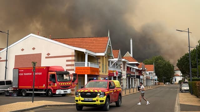Un camion de pompiers et un pick-up de secours dans une rue de Lège-Cap-Ferret, surmontés d'un immense panache de fumée noire de l'incendie du nord du bassin d'Arcachon.
