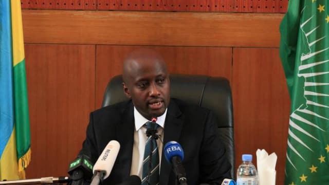 Olivier Nduhungirehe, ministre rwandais des Affaires étrangères, assis à une table de conférence de presse hérissée de micros, entre le drapeau du Rwanda et celui de l'Union africaine.
