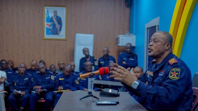 Un officier supérieur de la Police nationale congolaise, en uniforme sombre, s'exprime au micro derrière une table face à des rangées de policiers assis prenant des notes, sous le portrait du chef de l'État, lors d'un briefing sur la lutte contre le banditisme urbain à Kinshasa.