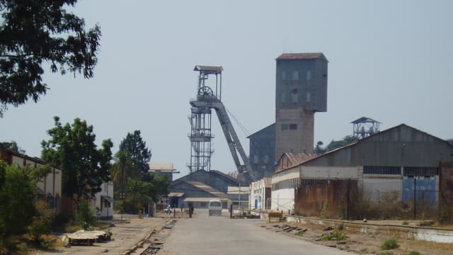Chevalement metallique et batiments industriels de la mine de cuivre de Kamoto, a Kolwezi, le long d une route bordee de voies ferrees.