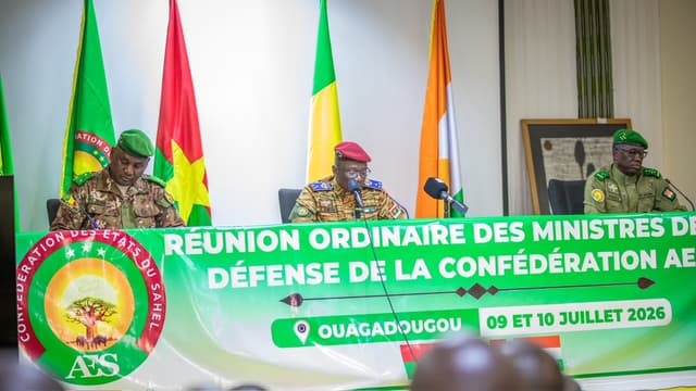Trois officiers généraux en tenue de camouflage siègent à la tribune d'une salle de conférence, devant les drapeaux du Burkina Faso, du Mali et du Niger et une banderole verte de la Confédération des États du Sahel.