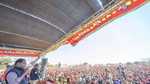 Le président zambien Hakainde Hichilema, micro en main sur une estrade ornée de banderoles rouges de l'UPND, salue une foule immense de partisans lors d'un meeting de campagne.
