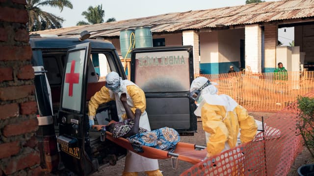 Deux soignants en combinaison de protection jaune transportent sur un brancard un patient sorti d'une ambulance, à l'entrée du centre de traitement Ebola de l'hôpital général de Mongbwalu, en Ituri.