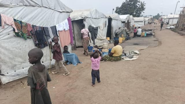 Vue d'un site de déplacés en Ituri, abris de fortune couverts de bâches et de pailles au milieu d'un terrain découvert