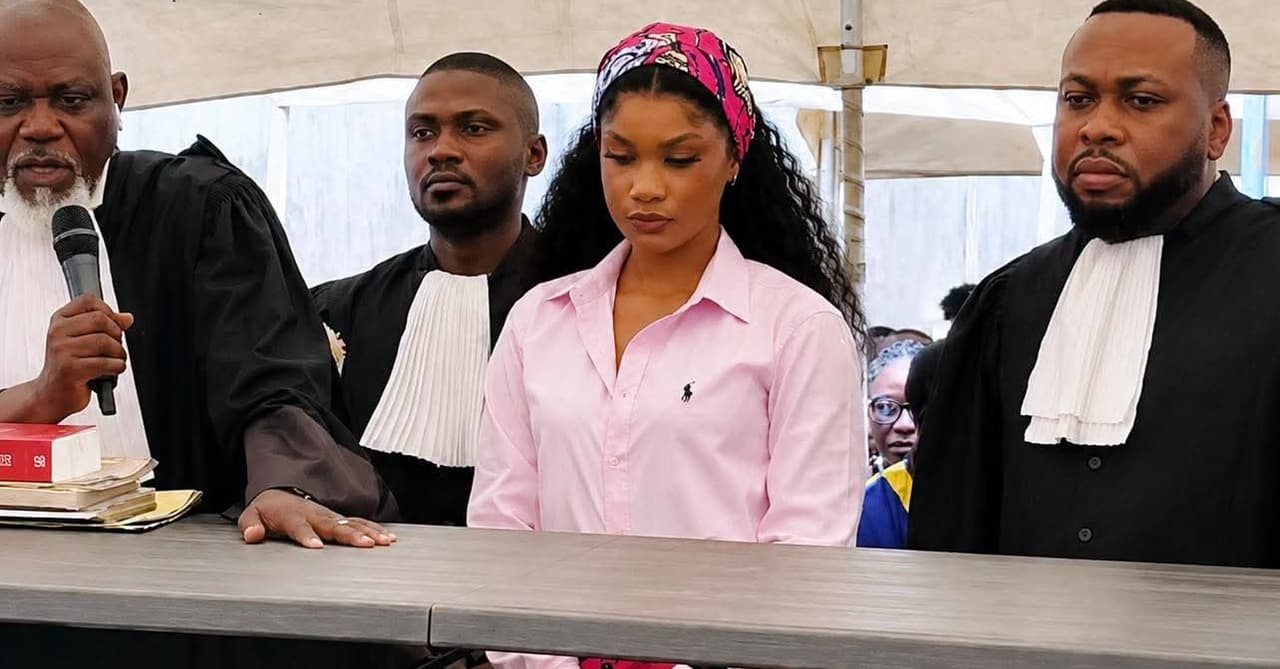 La chanteuse Rebo Tchulo, chemise rose et foulard fleuri, se tient debout derrière une table entre ses avocats en robe noire lors d'une audience du tribunal militaire.