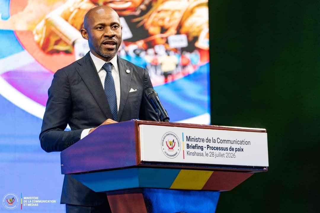 Patrick Muyaya, ministre de la Communication et porte-parole du gouvernement congolais, s'exprime au micro derrière un pupitre portant la mention « Ministère de la Communication, Briefing - Processus de paix, Kinshasa, le 28 juillet 2026 ».