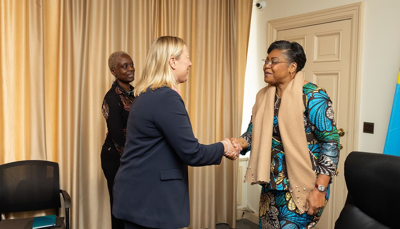 La Première ministre congolaise Judith Suminwa, à droite, serre la main de la commissaire européenne Jutta Urpilainen dans un salon de l'ambassade de la RDC à Bruxelles. Le drapeau congolais est visible à l'arrière-plan.