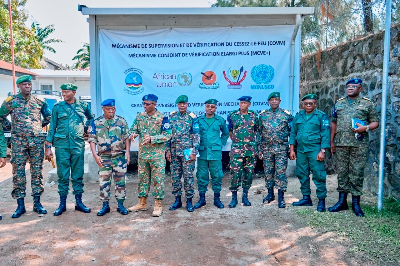 Une quinzaine d'officiers en tenues militaires différentes, dont plusieurs portant le béret bleu de l'ONU et des bérets verts, alignés devant une banderole blanche portant l'inscription « Mécanisme de supervision et de vérification du cessez-le-feu (COVM) , Mécanisme conjoint de vérification élargi plus (MCVE+) » et les logos de la CIRGL, de l'Union africaine, de l'Alliance Fleuve Congo, des FARDC et de la MONUSCO, dans une cour en terre battue à Goma.
