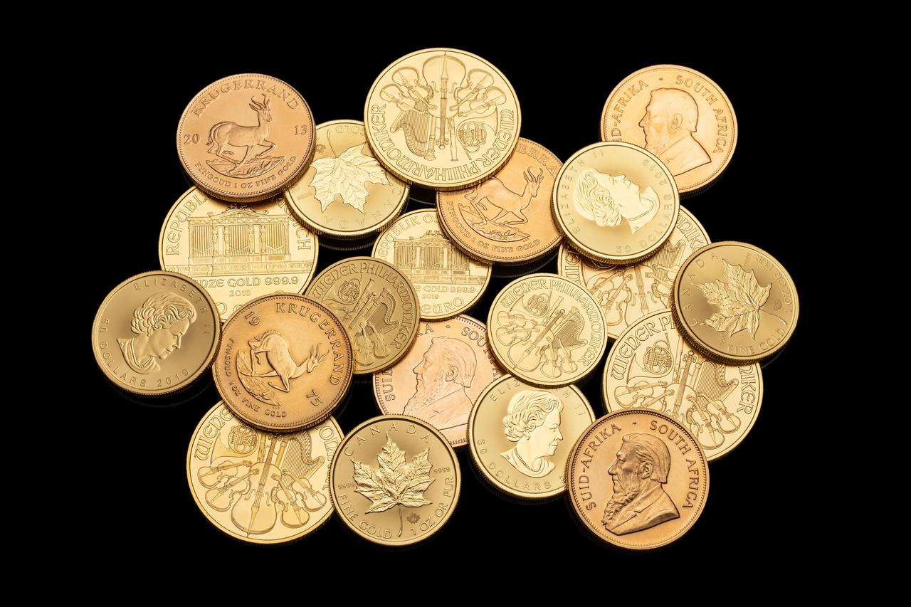 Une vingtaine de pièces d'or d'investissement (Krugerrand, Maple Leaf canadienne, Wiener Philharmoniker) posées en tas sur un fond noir
