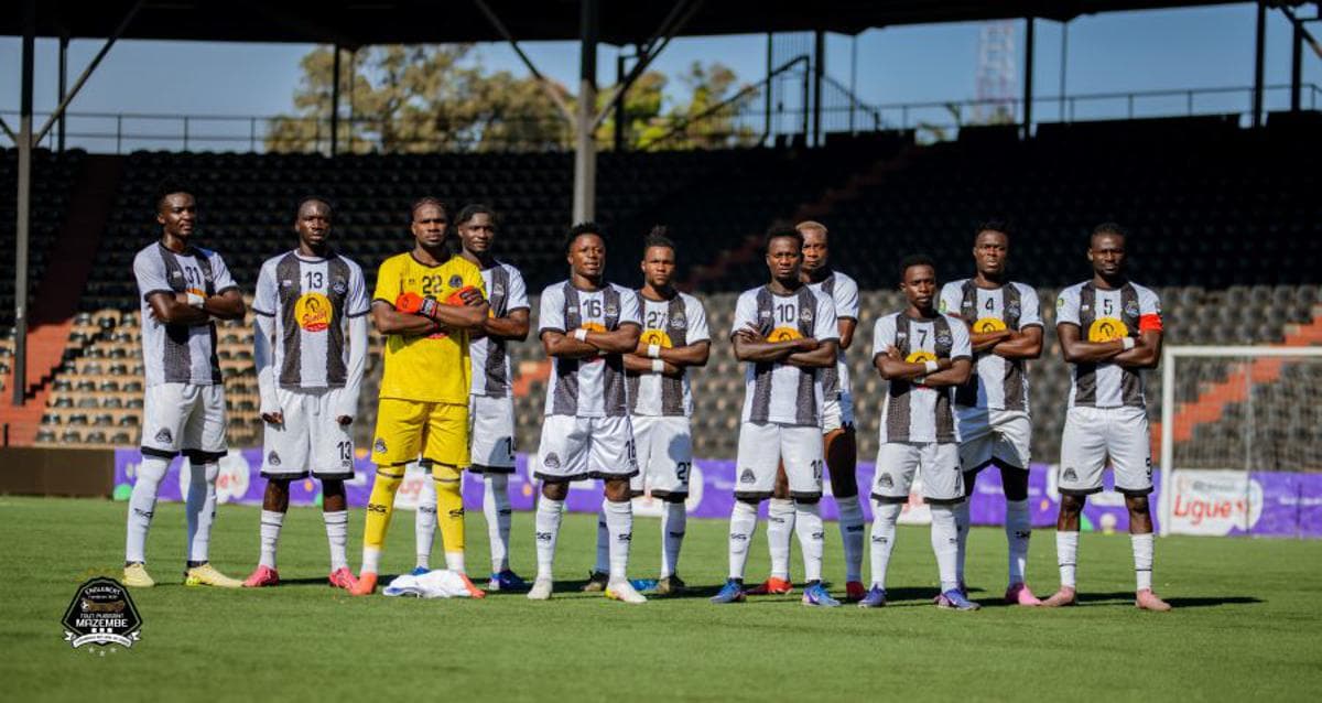 Le onze de départ du TP Mazembe, en maillot rayé noir et blanc, posant bras croisés sur la pelouse de leur stade à Lubumbashi avant un match.