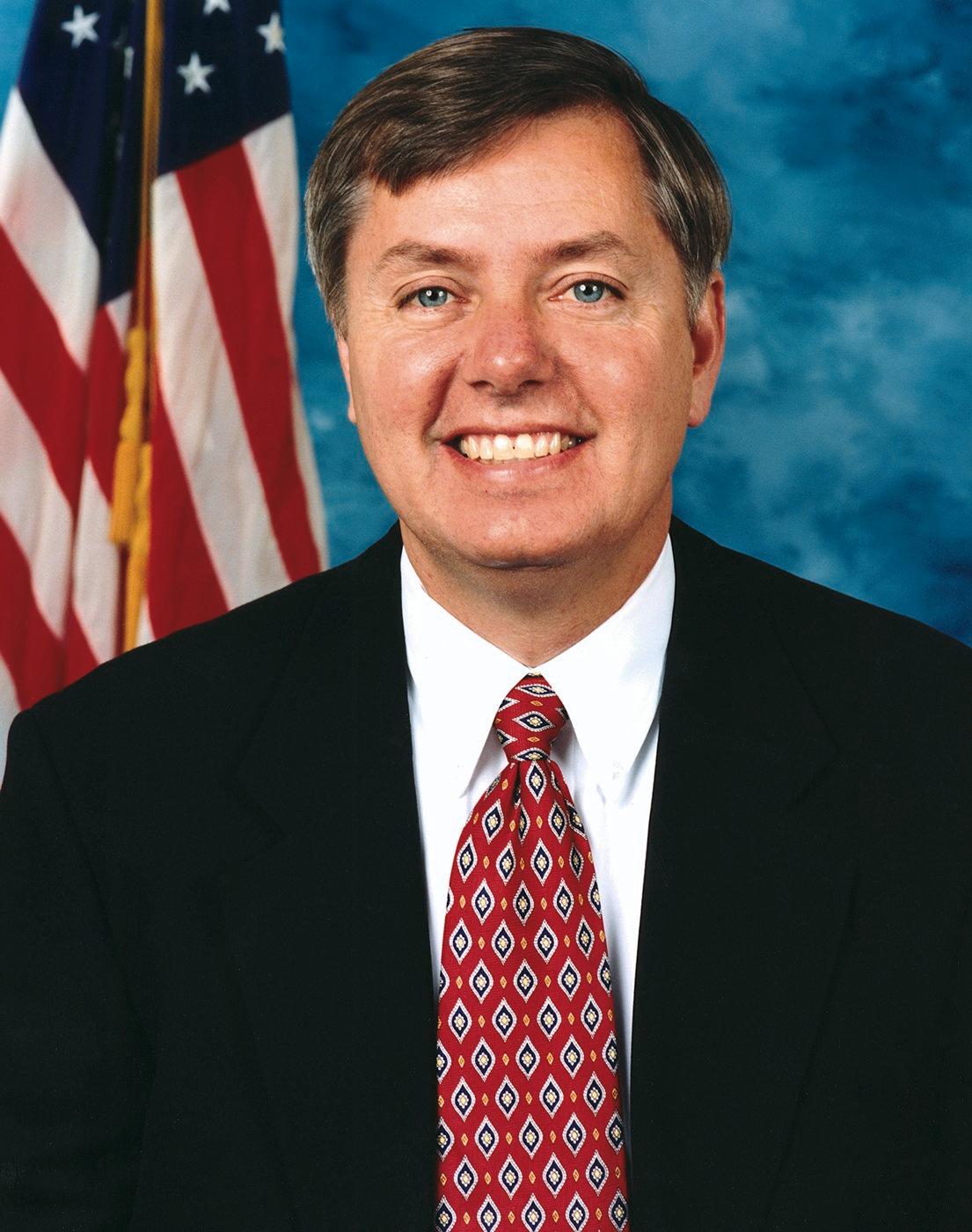 Portrait officiel du sénateur américain Lindsey Graham, en costume sombre et cravate, devant les drapeaux des États-Unis