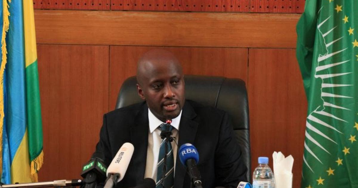 Olivier Nduhungirehe, ministre rwandais des Affaires étrangères, assis à une table de conférence de presse hérissée de micros, entre le drapeau du Rwanda et celui de l'Union africaine.