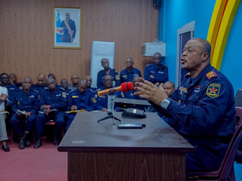 Un officier supérieur de la Police nationale congolaise, en uniforme sombre, s'exprime au micro derrière une table face à des rangées de policiers assis prenant des notes, sous le portrait du chef de l'État, lors d'un briefing sur la lutte contre le banditisme urbain à Kinshasa.