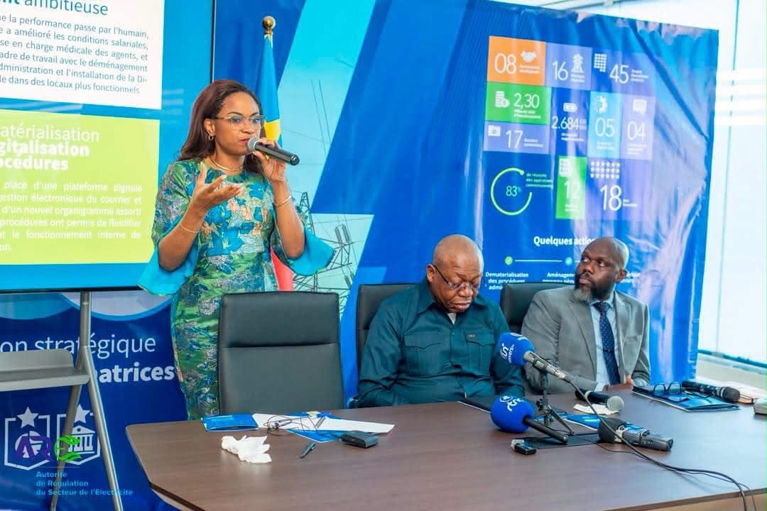 Soraya Aziz-Moto, directrice générale de l'ARE, s'exprime au micro lors du briefing des 100 jours, devant le logo de l'Autorité de régulation du secteur de l'électricité et un tableau de bilan affichant 2,30 milliards USD d'investissements et 45 projets énergétiques.