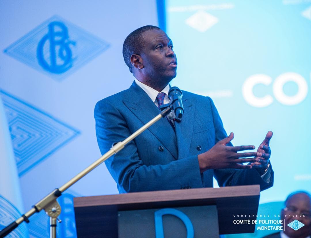 André Wameso, gouverneur de la Banque centrale du Congo, s'exprime debout au pupitre devant un micro lors d'une conférence de presse du Comité de politique monétaire, le logo de la BCC projeté derrière lui