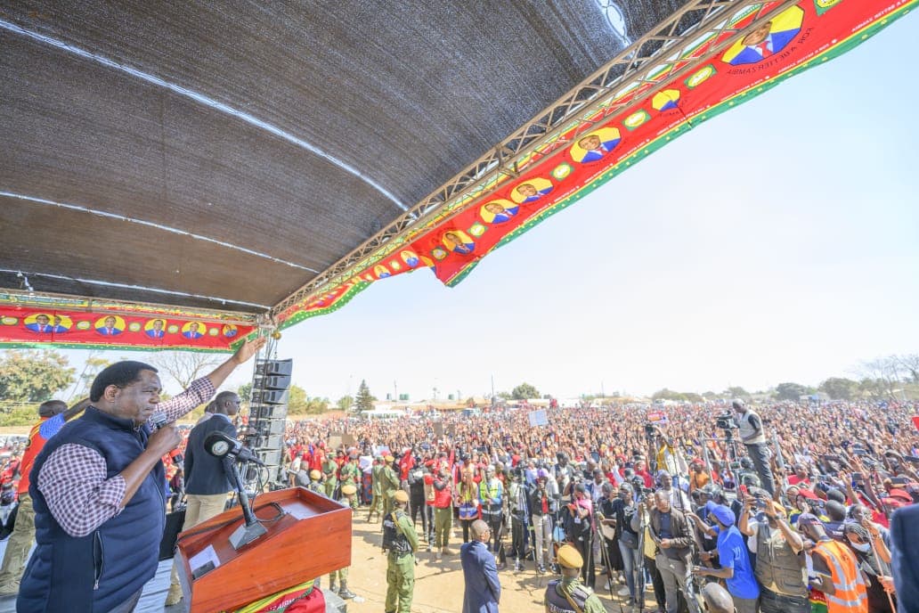 Le président zambien Hakainde Hichilema, micro en main sur une estrade ornée de banderoles rouges de l'UPND, salue une foule immense de partisans lors d'un meeting de campagne.