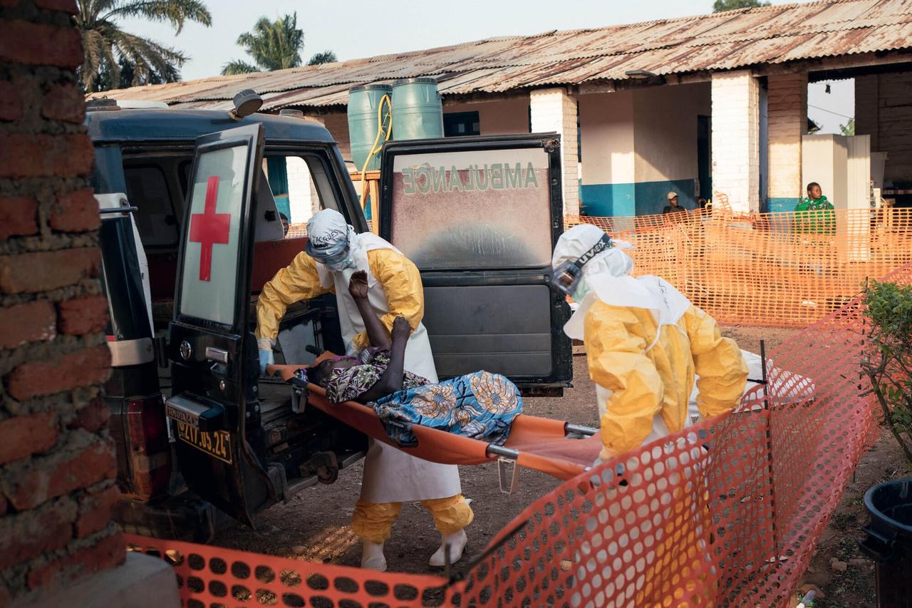 Deux soignants en combinaison de protection jaune transportent sur un brancard un patient sorti d'une ambulance, à l'entrée du centre de traitement Ebola de l'hôpital général de Mongbwalu, en Ituri.