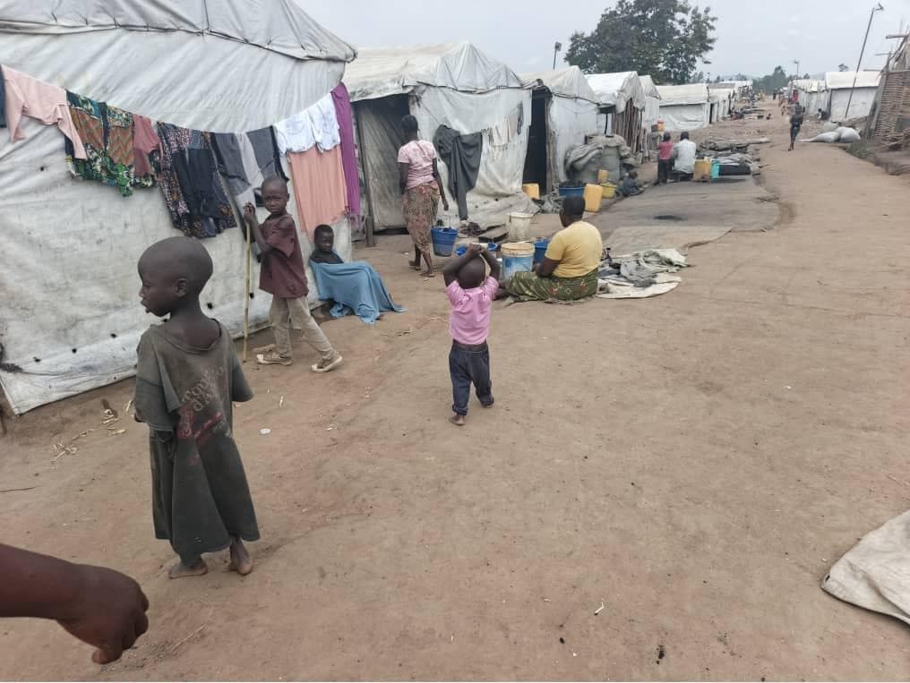Vue d'un site de déplacés en Ituri, abris de fortune couverts de bâches et de pailles au milieu d'un terrain découvert