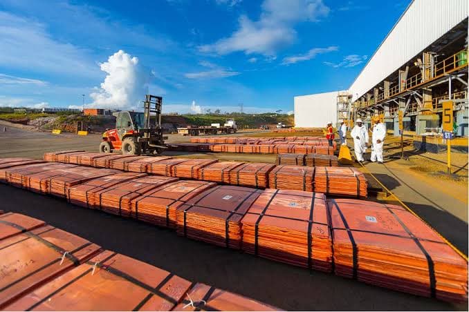 Piles de cathodes de cuivre alignées sur l'aire d'expédition de la mine de Tenke Fungurume, avec un chariot élévateur et des ouvriers en combinaison blanche